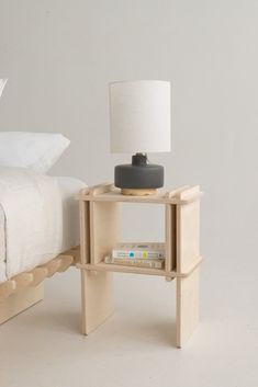 a nightstand with a lamp on top of it next to a bed in a white room