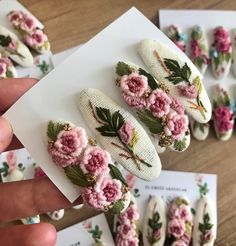 a person holding up some fake flowers on top of a piece of white paper with pink and green leaves