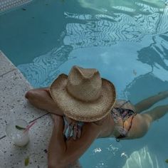 a woman wearing a straw hat sitting next to a swimming pool