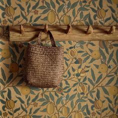 a woven bag hanging on a wall next to a wooden coat rack with hooks in it