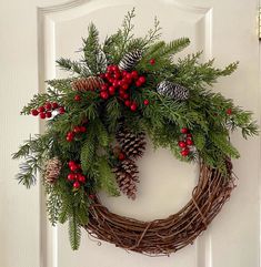 a wreath with pine cones and berries hanging on a door