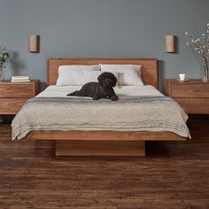 a black dog laying on top of a bed next to a wooden dresser and night stand