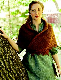 a woman standing next to a tree wearing a shawl and holding onto the trunk