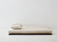 a bed with two pillows on top of it in front of a white wall and floor