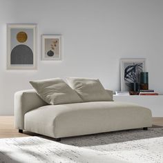 a white couch sitting on top of a wooden floor next to a wall with pictures above it