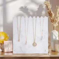 three necklaces are displayed on a table next to a vase with dried flowers in it