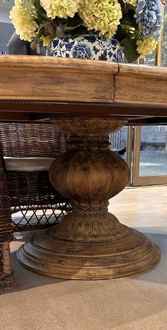 a wooden table with flowers on it in front of a glass door and some wicker chairs