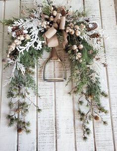 a wreath with pine cones and evergreens hanging on a white wooden wall in front of a door