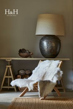 an animal hide chair in front of a table with a lamp and other items on it