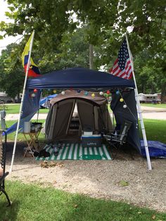 a tent set up in the middle of a park with two flags flying from it