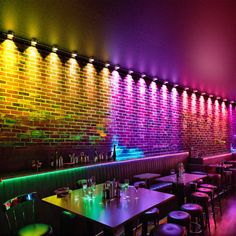 an empty restaurant with colorful lights on the brick wall and tables in front of it