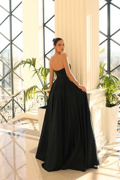 a woman in a long black dress leaning against a pillar with her back turned to the camera