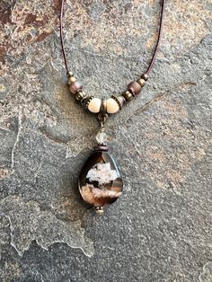 This beautiful Cherry Blossom Agate gemstone necklace is hung on a brown leather cord with natural wood beads, czech rustic glass beads and bronze metal accents. Light weight, simple and unique. Quality gift idea or something special for yourself. *I do not like it when I wear a necklace and my clasp eventually shifts to the front. This necklace, the clasp will stay in the back.  *The other necklace in the photos should be in my shop unless sold.  Details:  Cherry Bloosom Agate oval gemstone Natural wood beads 6mm Natural golden rutilated quartz faceted gemstone 4mm Glass beads Bronze metal spacers and beads Brown distressed genuine leather cord 1mm (thin) Bronze lobster clasp Length: leather cord is 16", pendant length is 1 1/2". I can add a 2" extension chain to make necklace 18", put in Adjustable Brown Beaded Necklaces Nature-inspired, Handmade Brown Agate Crystal Necklace, Brown Natural Stones Necklace For Festival, Bohemian Brown Pendant Crystal Necklace, Unique Handmade Brown Crystal Necklace, Nature-inspired Brown Beaded Necklaces, Unique Brown Teardrop Necklace, Brown Beaded Teardrop Necklace, Beaded Teardrop Brown Necklace