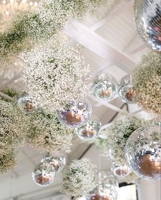 several disco balls hanging from the ceiling with baby's breath flowers on them in front of a mirror ball chandelier