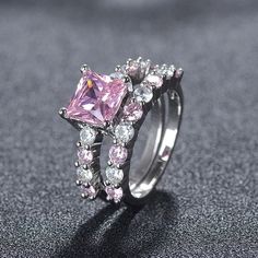 a pink diamond ring set on top of a black surface with diamonds around the band