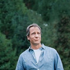 a man standing in front of trees with his hands on his hips and looking at the camera