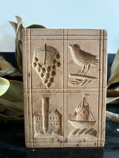 a ceramic block with birds, buildings and grapes on it sitting next to some plants