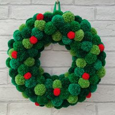 a green wreath with red and green pom - poms hanging on a brick wall