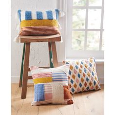 two multicolored pillows sitting on top of a wooden stool next to a window