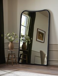 a mirror sitting on top of a wooden floor next to a vase with flowers in it