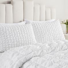 a bed with white sheets and pillows on top of it next to a vase filled with flowers