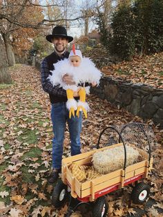 a man holding a baby in his arms while standing next to a wagon filled with hay