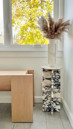 a vase with some plants in it sitting next to a table and window sill