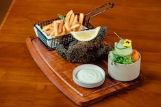 a wooden tray topped with food next to a container of ranch dressing and french fries