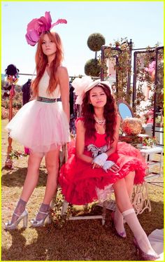 two women in dresses and hats sitting on a bench