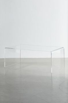 a clear table sitting on top of a floor next to a white wall and chair