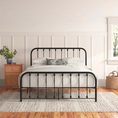 a bedroom with white walls and wood flooring has a black iron bed frame on top of it