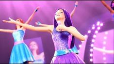 barbie the little mermaid singing on stage with her hands in the air and other dancers behind her