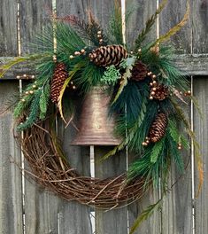 a christmas wreath with pine cones, evergreens and bells hanging on a wooden fence