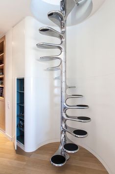 a modern spiral staircase in the middle of a room with white walls and wood flooring