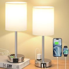 two lamps sitting on top of a wooden table next to a phone and charger