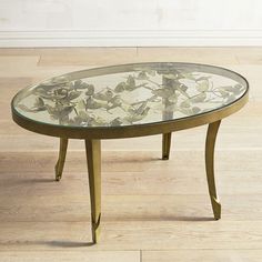 an oval glass table with metal legs and flowers on the top, sitting on a wood floor