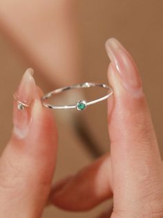 a close up of a person's hand holding a ring with a green stone