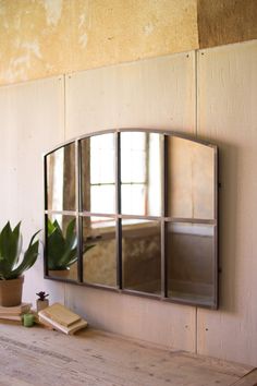 a mirror on the wall above a wooden table with a potted plant and books