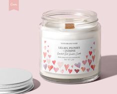 a white candle with hearts on it next to a pink background and a silver lid