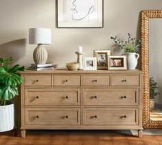 a dresser with many drawers and pictures on the top, next to a large mirror