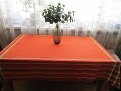 a vase with some flowers sitting on top of a red table cloth in front of a window