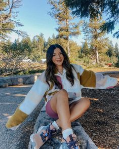 a woman sitting on top of a rock next to trees