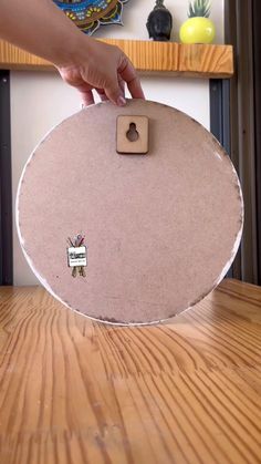 a person holding a round object on top of a wooden table next to a shelf