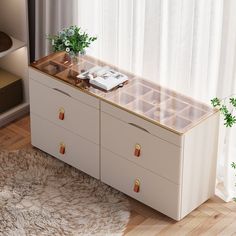 a white dresser with drawers and plants on it in front of a curtained window