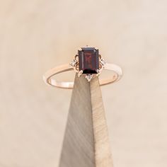 an engagement ring with a garnet colored stone sits on top of a piece of wood