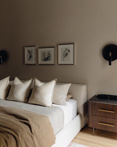 a bed with four pillows on top of it and two pictures above the headboard