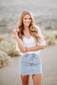 a beautiful young woman posing in the middle of a road with her arms crossed and smiling