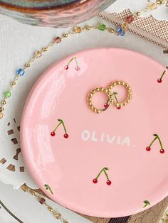 a pink plate with two wedding rings on it and the word oliva written in gold