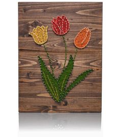 three flowers made out of beads sitting on top of a wooden wall mounted plaque with green leaves