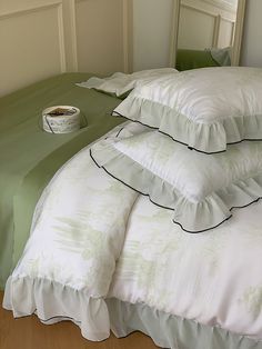 a bed with green sheets and pillows on top of it, next to a cup of coffee